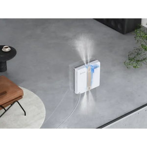 Ecovacs Winbot Mini white and beige robot window vacuum in action spraying water mist on an outdoor patio window with concrete flooring and garden furniture visible