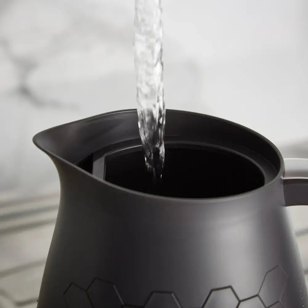 Water pouring into a black Morphy Richards Cassini jug kettle with a geometric hexagon pattern design on a white kitchen surface
