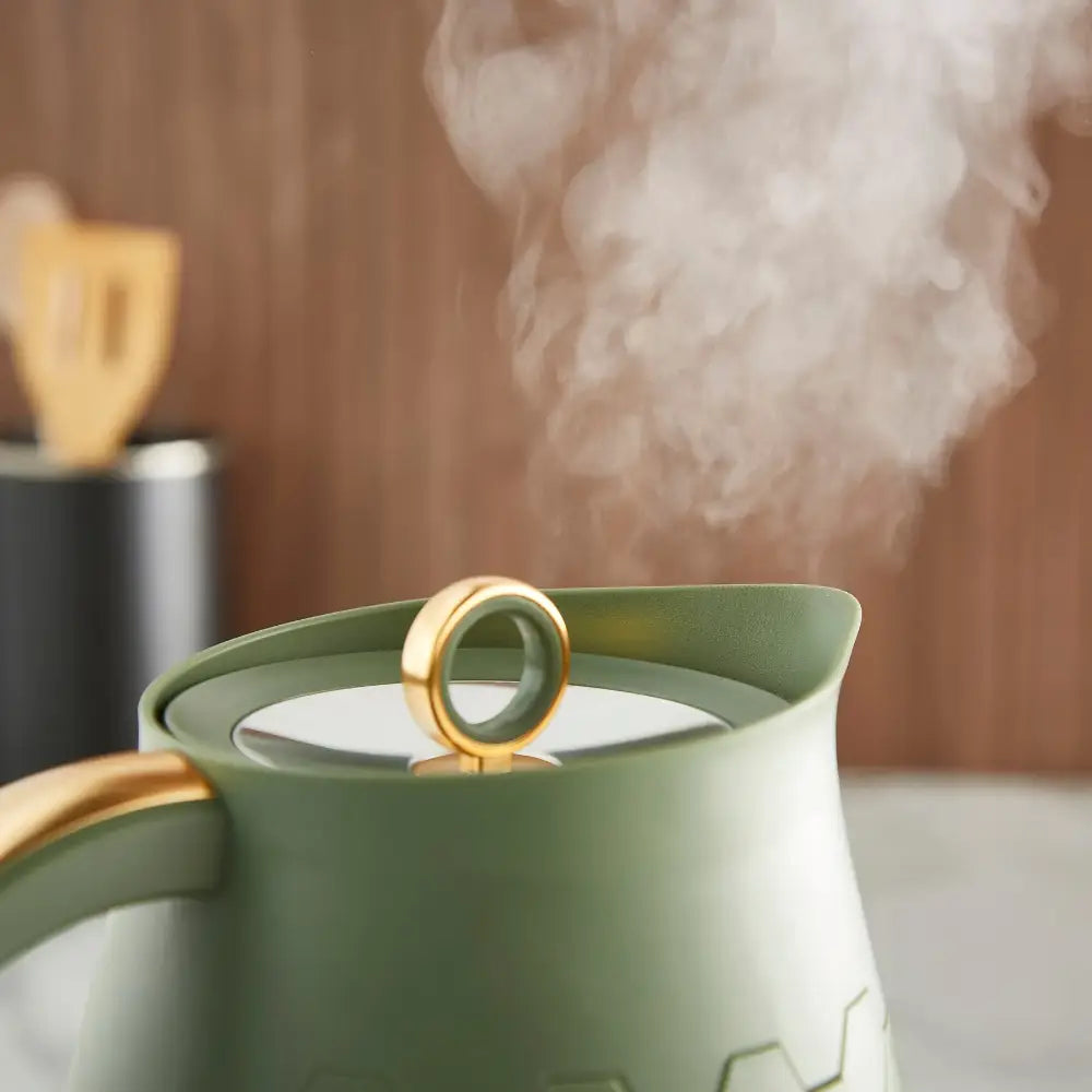 Morphy Richards Cassini jug kettle in olivine green with gold accents, steaming with white vapor, featuring a gold-trimmed lid and handle against a warm neutral background