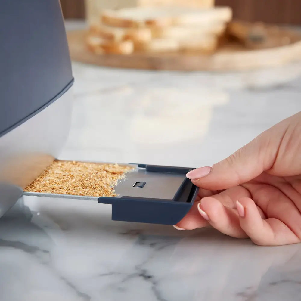 Hand holding a slice of golden brown toast near the chrome slot of a Morphy Richards Cassini 4 Slice Toaster in Outer Space grey finish, with marble countertop and blurred kitchen items in background
