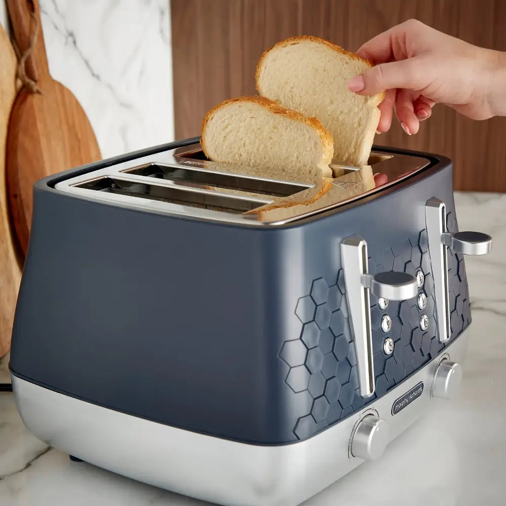 Morphy Richards Cassini 4 slice toaster in grey and white with two slices of toasted bread being removed, showing hexagonal texture detail on the body and chrome accents on a marble countertop