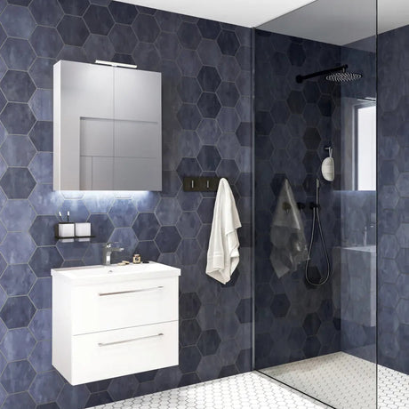 Modern bathroom with wall-hung white vanity unit featuring two drawers and integrated sink, illuminated mirror cabinet above, dark hexagonal tile walls, glass shower enclosure with black fixtures, and white hexagonal floor tiles