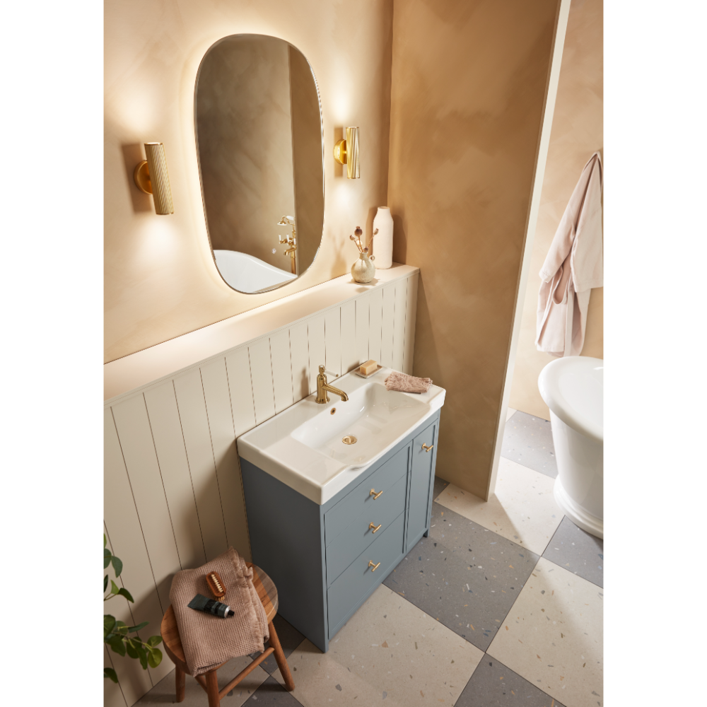 Modern bathroom vanity unit featuring a Roper Rhodes Concierge basin in matt Coniston blue with white ceramic sink, brass tap and handles, paired with an oval illuminated mirror, white shiplap panelling, warm beige walls, brass wall sconces, terrazzo flooring, and coordinating accessories in a contemporary spa-like setting