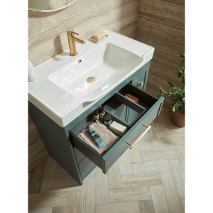 Roper Rhodes Concierge vanity unit with white ceramic basin, matt coniston blue cabinet, brass tap, open drawer displaying toiletries and towels, herringbone wood flooring, stone tile walls, modern bathroom setting
