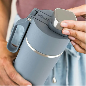 Ninja Thirsti 530ml insulated travel bottle in tropical blue with stainless steel accents, featuring a gray handle and lid, held in hands against a blurred background