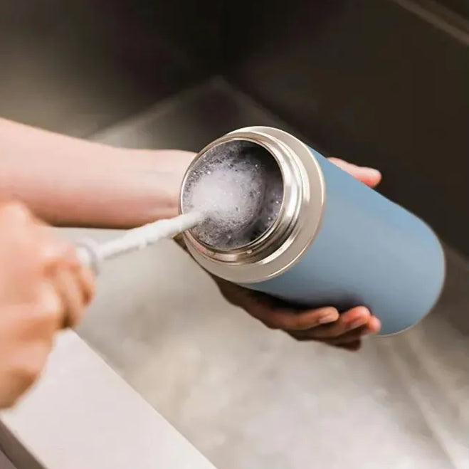 Hand holding open Ninja Thirsti 530ml insulated travel bottle in tropical blue showing interior with ice cubes and stainless steel cap