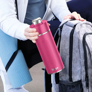 Person holding a hot pink Ninja Thirsti 530ml insulated travel bottle with stainless steel top next to a grey backpack, wearing white and blue clothing