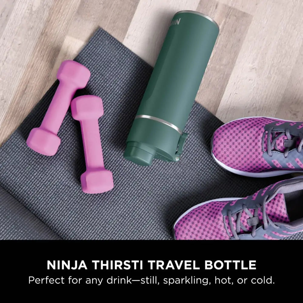 Ninja Thirsti 700ml insulated travel bottle in evergreen green displayed on gray yoga mat with pink dumbbells and purple running shoes for fitness lifestyle setup