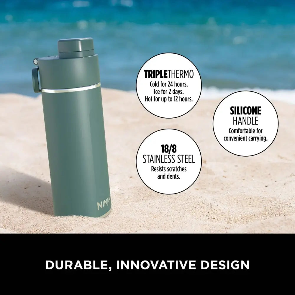 Ninja Thirsti 700ml insulated travel bottle in evergreen color displayed on beach sand with ocean background, featuring triple thermo technology keeping drinks cold for 24 hours or hot for 12 hours, silicone handle for carrying, and 18/8 stainless steel construction