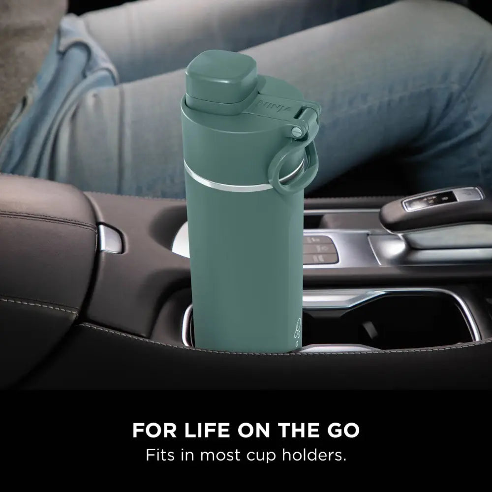 Ninja Thirsti 700ml insulated travel bottle in evergreen green colour positioned in a car cup holder, featuring a secure lid with carry handle and stainless steel band, displayed in a vehicle interior setting with the tagline "For life on the go - Fits in most cup holders"