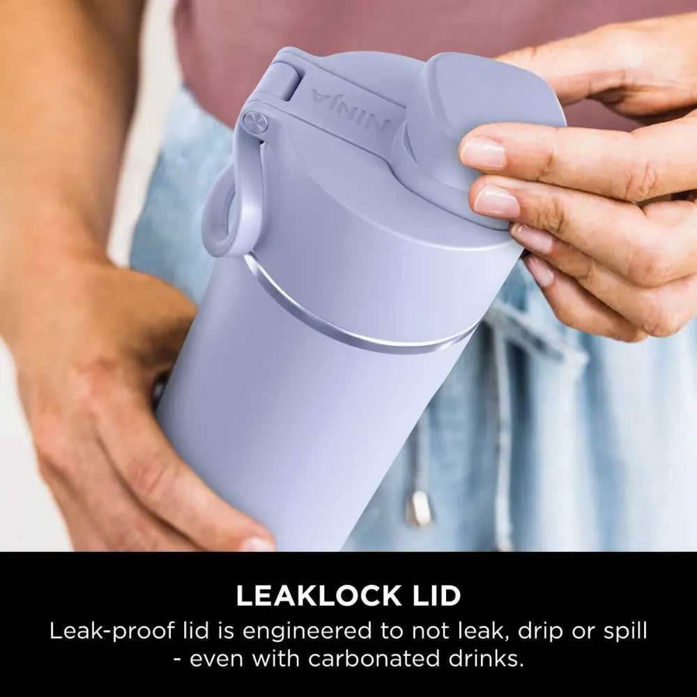 Person holding a lavender-colored Ninja Thirsti 700ml insulated travel bottle demonstrating the LeakLock lid feature, with text describing leak-proof engineering for carbonated drinks