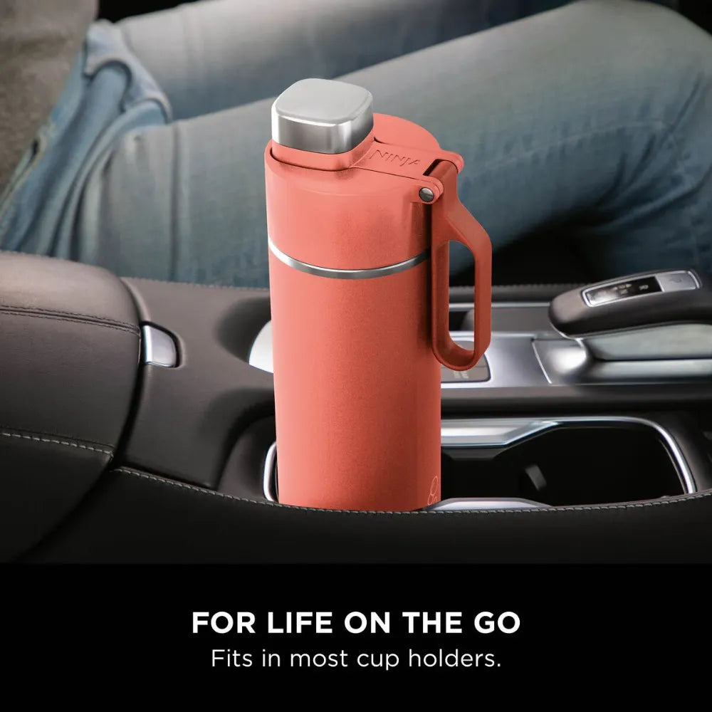 Coral red Ninja Thirsti 700ml insulated travel bottle with stainless steel cap and handle strap, displayed in a car cup holder between front seats