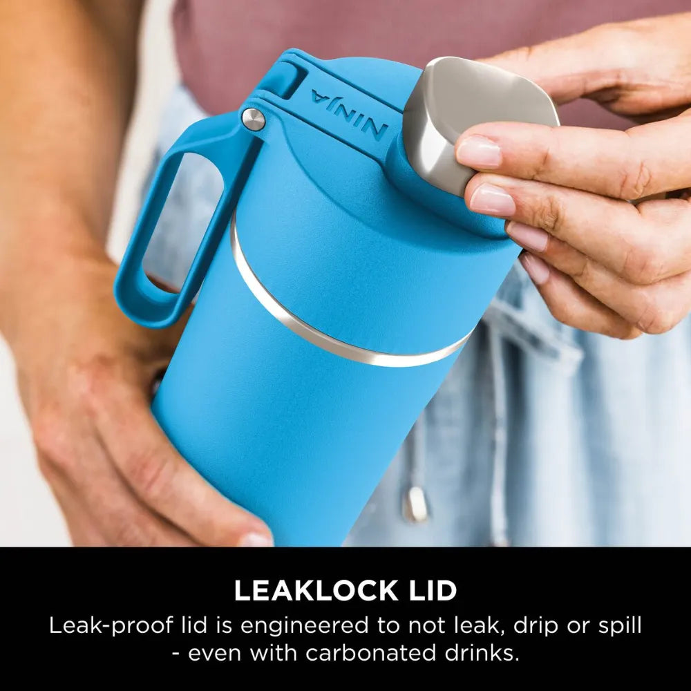 Hands holding a blue Ninja Thirsti 700ml insulated travel bottle with white accents and LeakLock lid, demonstrating the leak-proof design against a blurred background