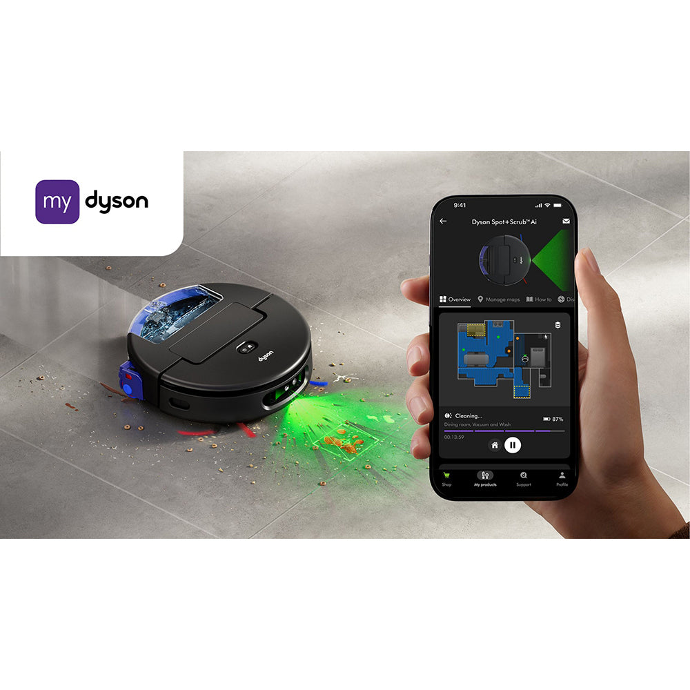 My Dyson app interface showing Dyson Spot+Scrub AI robot vacuum with green laser detection mapping a room, displayed on smartphone screen held in hand, with black robotic vacuum cleaner on tile floor surrounded by debris and cleaning solution visualization
