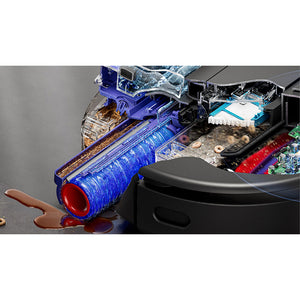 Dyson Spot+Scrub AI robot vacuum displayed with internal components visible, showing blue cylindrical brush, red end cap, black body, circuit boards, and water tank alongside brown liquid spillage demonstration on gray surface