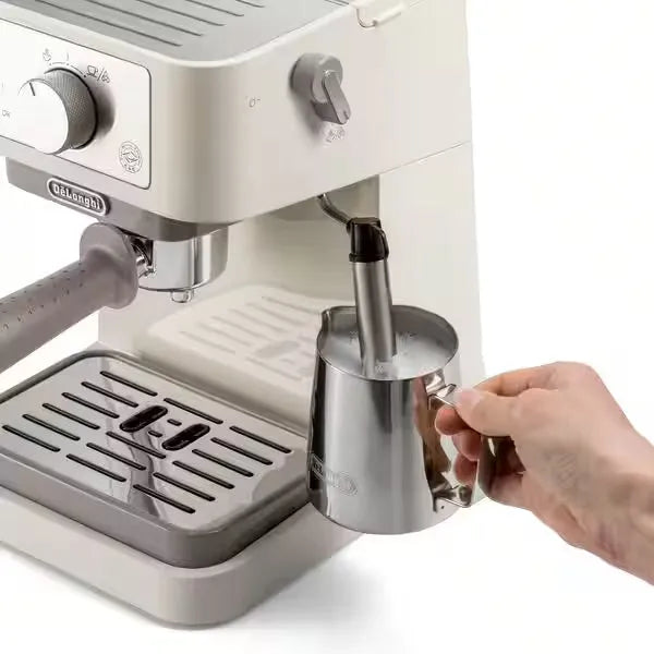 DeLonghi Stilosa cream espresso machine with stainless steel milk frother pitcher being held by hand, showing drip tray and control knobs