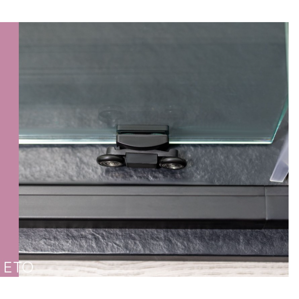 Close-up of Flair ETO sliding shower door hardware showing black frame with chrome handle and dual wheels mounted on glass panel against grey tiled bathroom wall