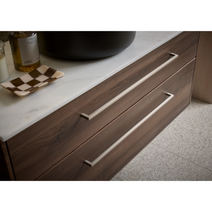 Dark walnut wood vanity unit with white marble countertop, chrome handles, and decorative items including wine bottle and checkered dish