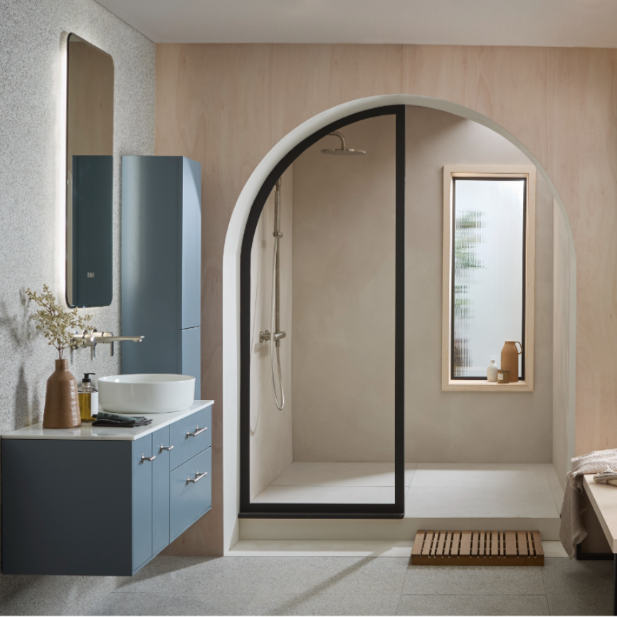Modern bathroom interior featuring a Coniston Blue vanity unit with white round basin sink, tall dark mirror, curved black-framed shower enclosure, wooden bath mat, and neutral beige tile and wood-paneled walls