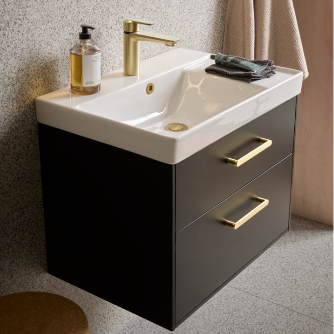 Black wall-mounted bathroom vanity unit with white ceramic sink, brass tap and handles, featuring two drawers and storage, styled with soap dispenser, towels and accessories