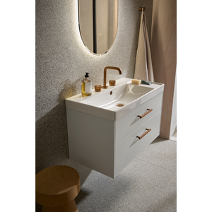 Modern white wall-mounted bathroom vanity unit with dual ceramic sink, brass faucet, two storage drawers with copper handles, illuminated oval mirror, terrazzo flooring, and beige towel rail