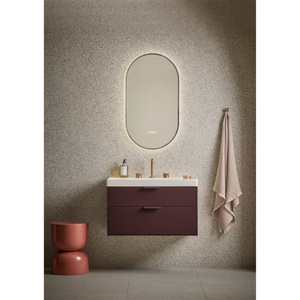 Modern bathroom vanity setup featuring a burgundy Roper Rhodes Faber wall-mounted vanity unit with white countertop and integrated sink, paired with an illuminated oval mirror with soft gold lighting, terracotta ceramic accessories, and neutral beige towel against textured taupe wall