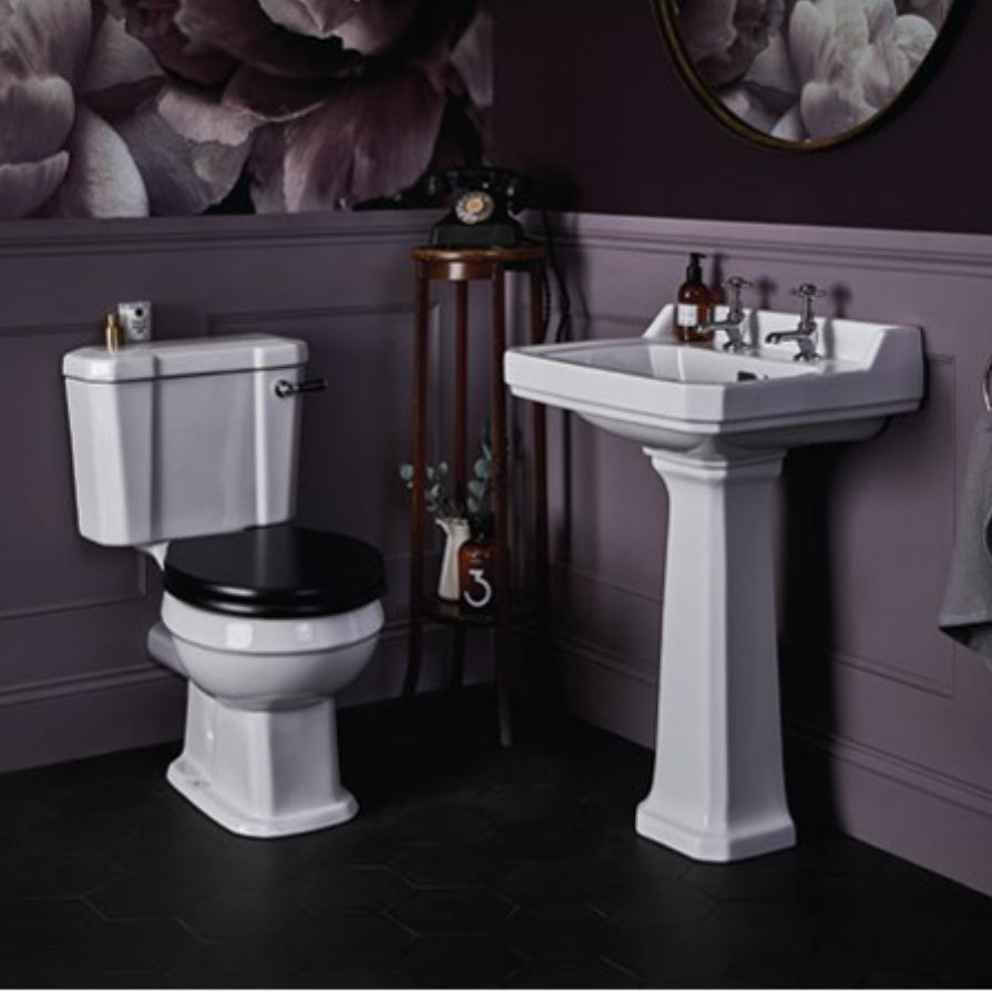 Bayswater Fitzroy white ceramic close coupled toilet with cistern and seat in a luxury bathroom setting with pedestal sink, purple walls, black floor and vintage accessories