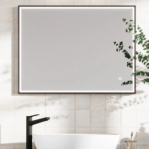 Modern LED bathroom mirror with black frame mounted on cream subway tiles above a white vessel sink and black faucet, featuring integrated lighting and trailing eucalyptus plant decoration
