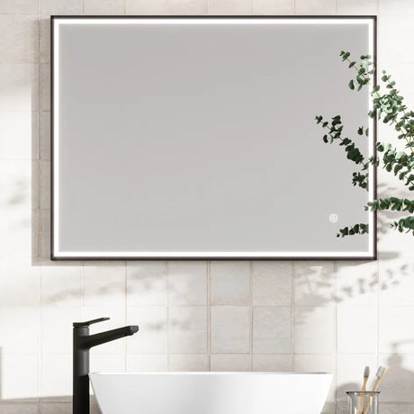 Modern LED bathroom mirror with black frame mounted on cream subway tiles above a white vessel sink and black faucet, featuring integrated lighting and trailing eucalyptus plant decoration