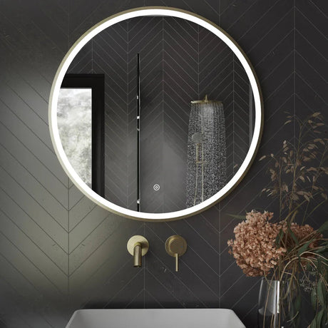Aqualla Fuse Frame Round LED Bathroom Mirror 700mm in black with brushed brass fixtures mounted on dark herringbone tile wall above white basin with rainfall showerhead visible in reflection