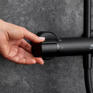 Hand demonstrating the rotating dual bar control of a Mira Relate matt black mixer shower valve mounted on a textured grey bathroom wall