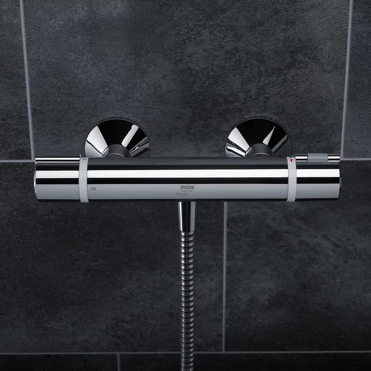 Mira Relate exposed bar mixer shower in polished chrome with dual circular controls mounted on dark grey tile wall with chrome flexible hose connection