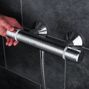 Mira Relate exposed bar mixer shower in polished chrome mounted on dark grey tile wall with water droplets on showerhead and hand adjusting controls