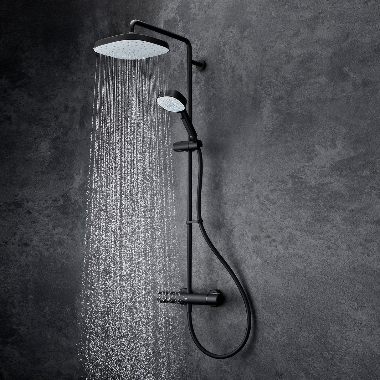 Mira Relate dual bar mixer shower in matt black with overhead rainfall showerhead and handheld spray, mounted on textured grey tile wall, water streams visible