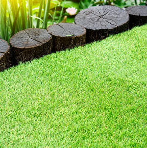 Close-up view of bright green Greenfx Capri artificial grass 28mm pile height with dark wooden log edging and garden plants in background