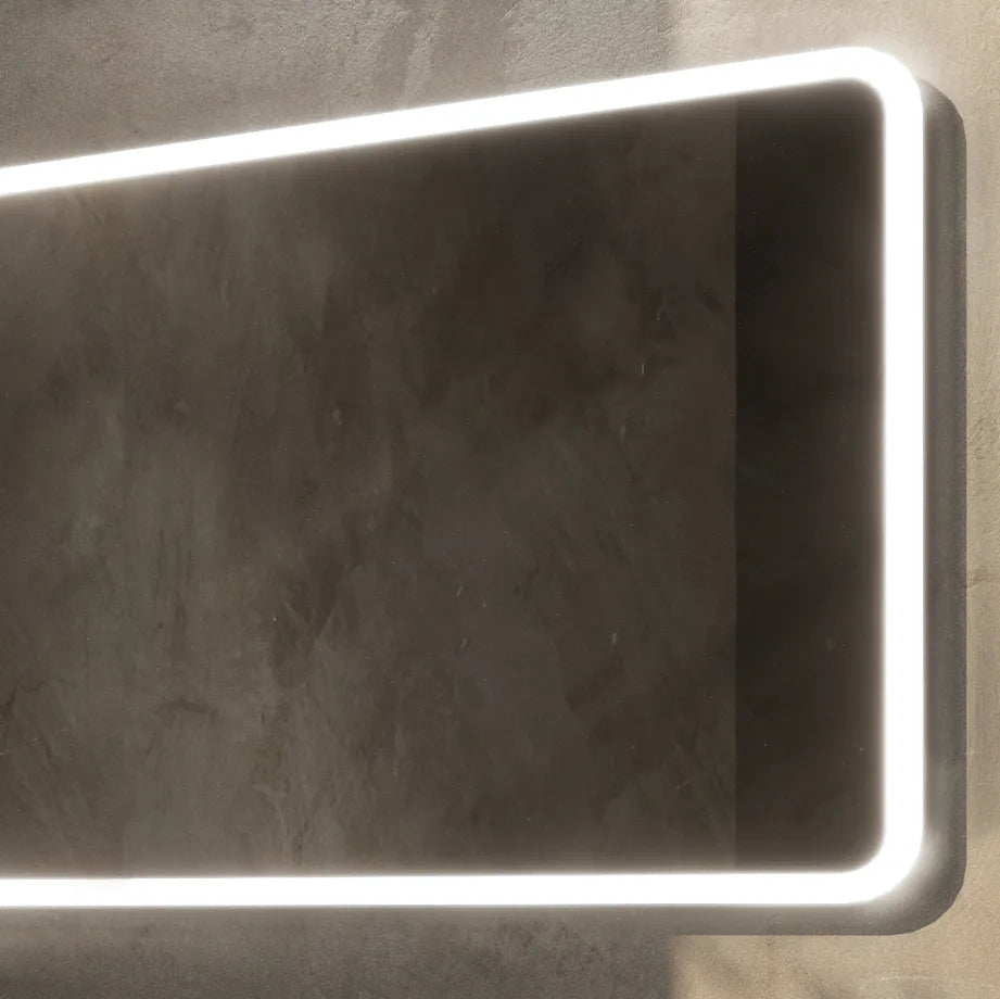 Modern Aqualla Glow LED bathroom mirror with white illuminated edge trim against textured grey concrete wall background, featuring rounded corners and sleek contemporary design