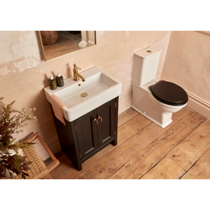 Modern bathroom vanity unit in Matt Black with white rectangular ceramic sink, brass tap, and black toilet seat, set on wooden flooring with pink walls and dried floral decoration