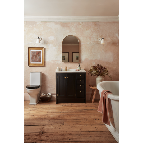 Roper Rhodes Hampton vanity unit in matt black with gold handles and white ceramic sink in a spa-style bathroom with wooden flooring, arched mirror, pendant lights, freestanding white bathtub and textured terracotta wall finish