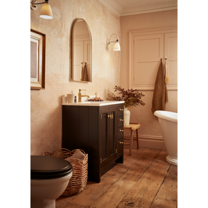 Matt Black Hampton vanity unit with white countertop in warm peach bathroom featuring wooden flooring, arched mirror, brass fixtures and traditional styling