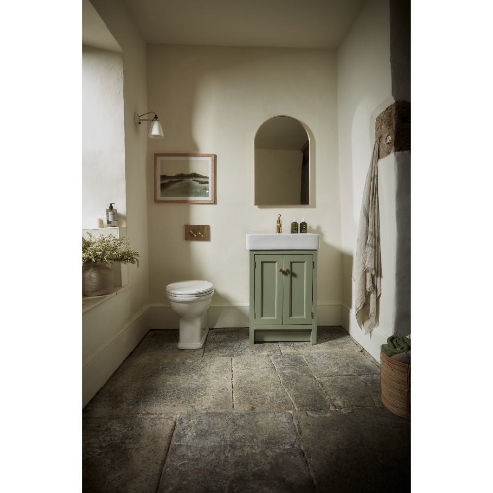 Sage green Hampton vanity unit with white ceramic sink in a neutral bathroom featuring slate grey stone flooring, arched mirror, and cream walls