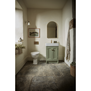 Sage green Hampton vanity unit with white ceramic sink in a neutral bathroom featuring slate grey stone flooring, arched mirror, and cream walls