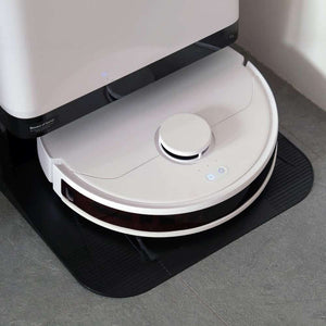 White and black robotic vacuum cleaner with circular disc design, dust collection bin on top, and control buttons, positioned on black mat against grey floor