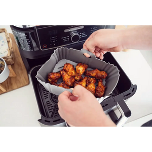 Person holding open a black air fryer basket containing cooked golden brown chicken pieces lined with a gray silicone air fryer liner, displaying the product in use
