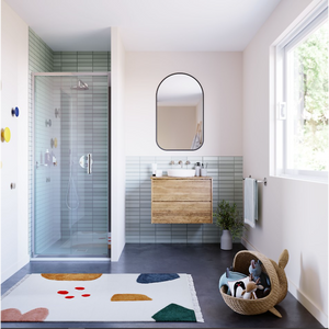Modern bathroom interior featuring Flair ILI chrome bifold shower door with light blue subway tiles, wooden vanity unit, arched black mirror, dark floor, and colorful bath mat