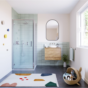Modern bathroom featuring Flair ILI chrome and matte black hinged shower door with light green subway tiles, wooden vanity with white basin, arched mirror, dark grey flooring, and decorative bath mat with geometric shapes