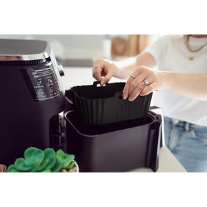 Woman in white shirt removing black silicone air fryer liner from air fryer basket, showing product functionality and size