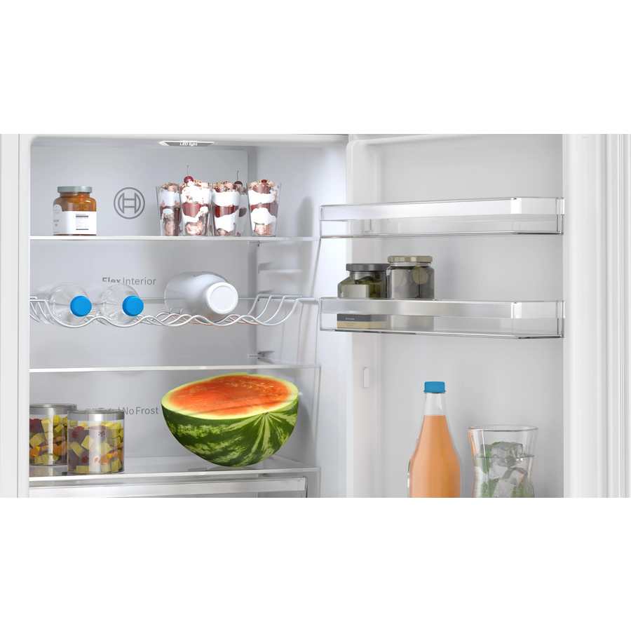 Open Bosch Series 4 white fridge freezer displaying organized interior with fresh watermelon, beverages, pickled vegetables, desserts in glass containers, and various groceries on shelves and door storage