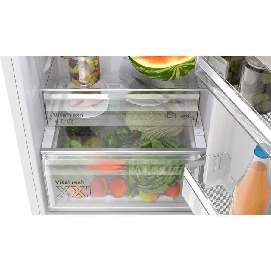 Interior view of a Bosch Series 4 white fridge freezer showing two VitaFresh drawers containing fresh vegetables including lettuce, tomatoes, cucumbers and a watermelon, with juice bottles visible on the right side door shelf