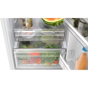 Interior view of a Bosch Series 4 white fridge freezer showing two VitaFresh drawers containing fresh vegetables including lettuce, tomatoes, cucumbers and a watermelon, with juice bottles visible on the right side door shelf