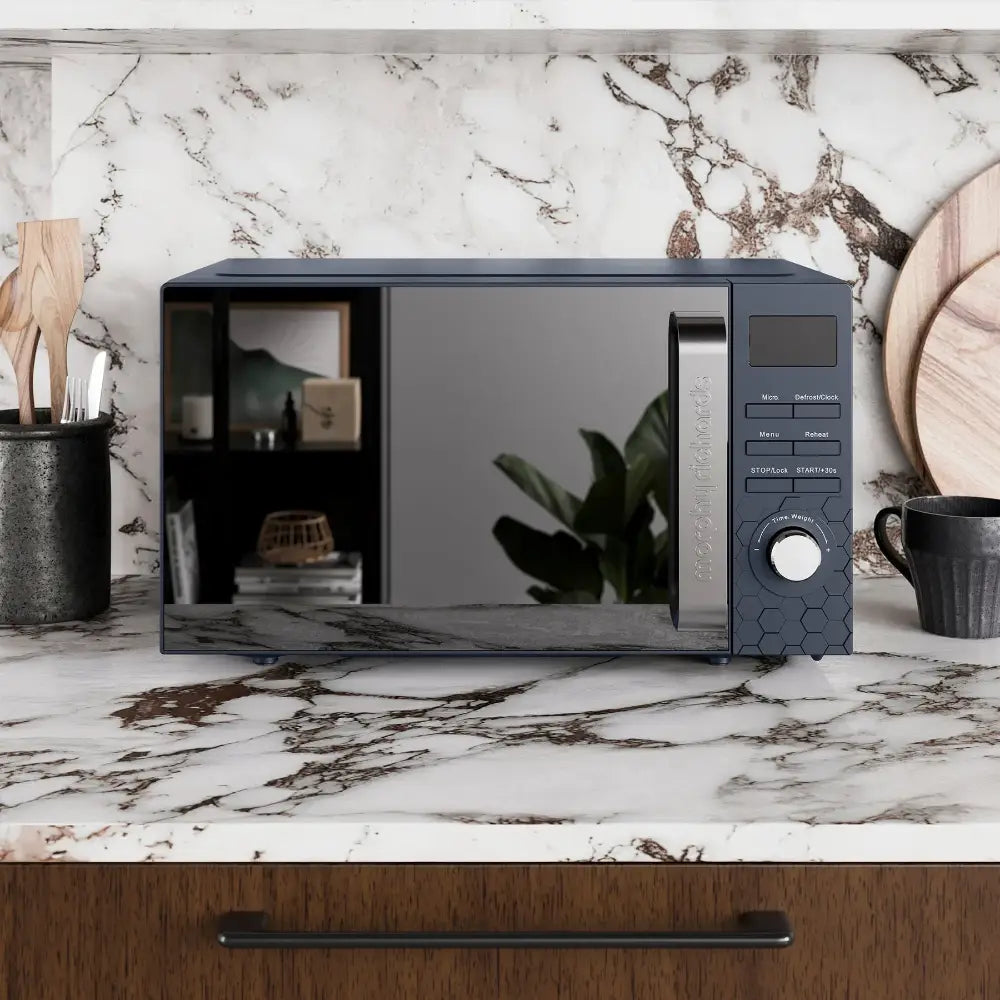 Morphy Richards Cassini Digital Microwave 20 Litre 700W in Outer Space grey displayed on a marble countertop with black accents, featuring digital controls, power dial, and reflective door next to black ceramic containers and wooden accessories in a modern kitchen setting